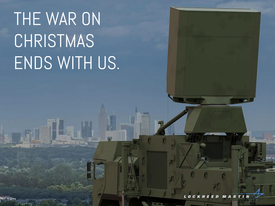 Lockheed Martin ad showing a large piece of military equipment on a hill overseeing a large, populous city. It's captioned "the war on Christmas ends with us."